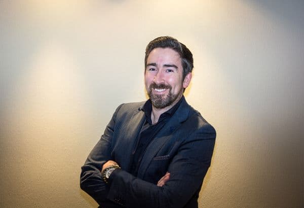 Smiling bearded man in a dark blazer with arms crossed