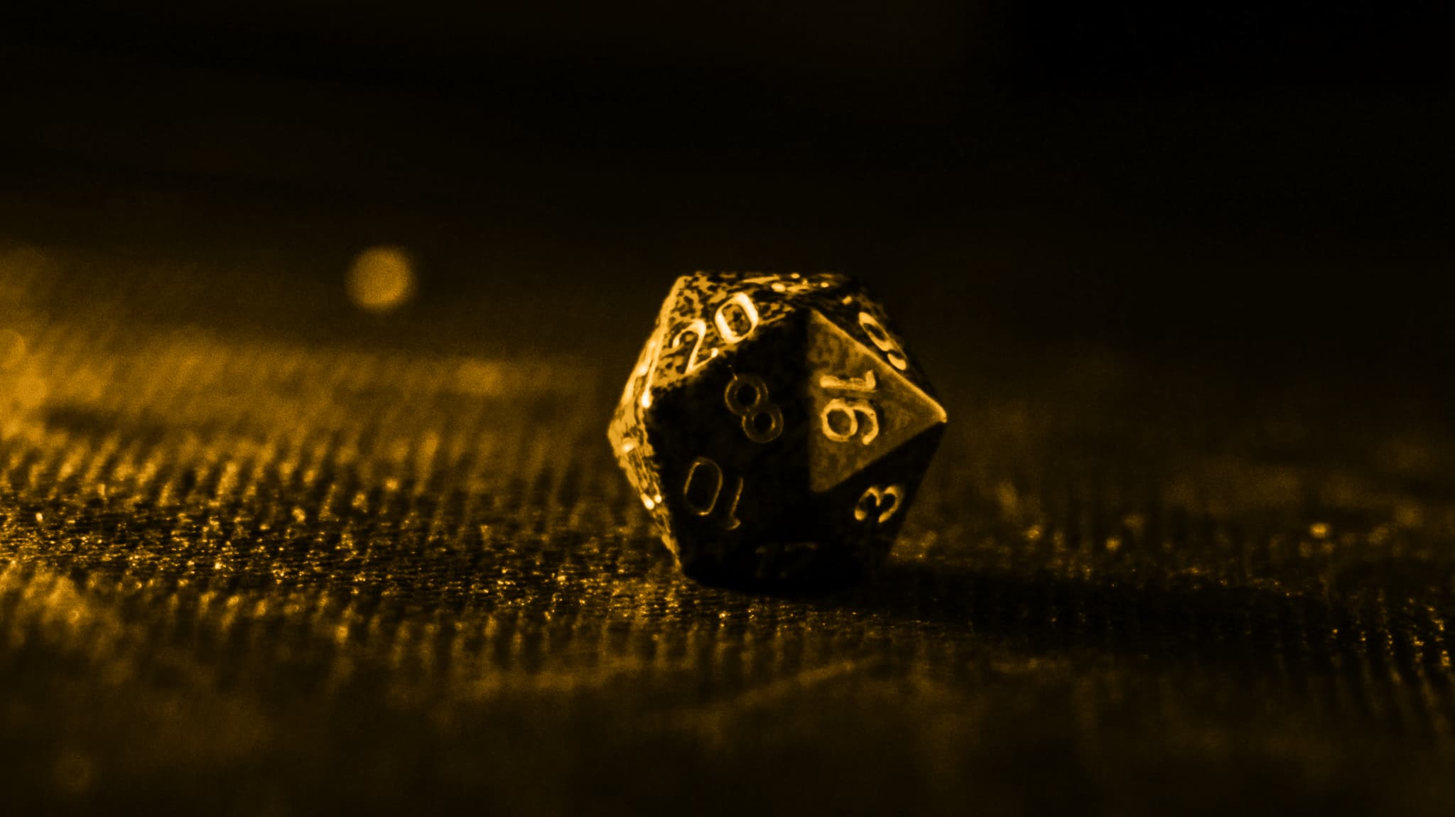 Twenty-sided die lit in gold on a dark surface, symbolising randomness