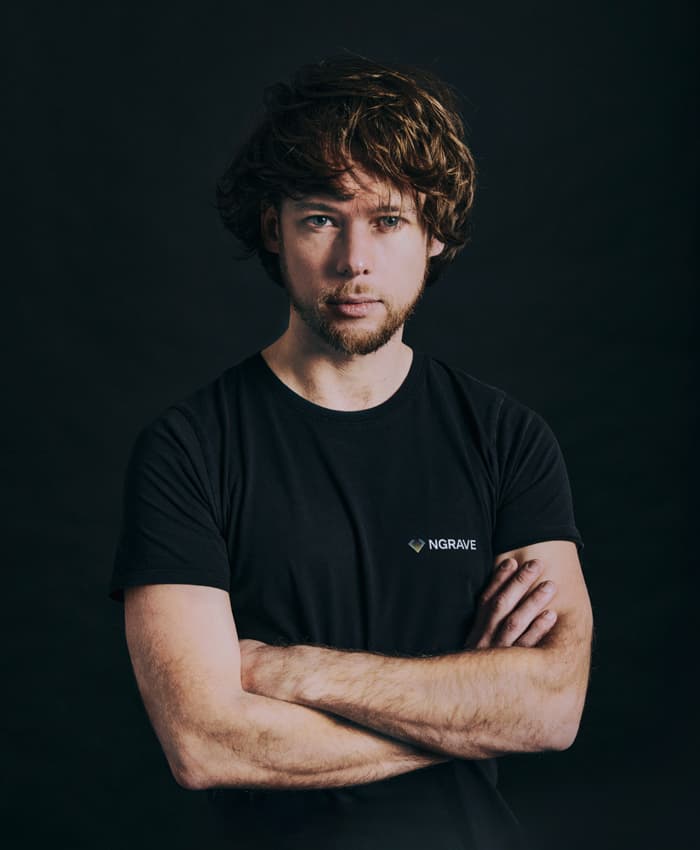 Portrait of a man with curly reddish hair in a black NGRAVE T-shirt, arms crossed